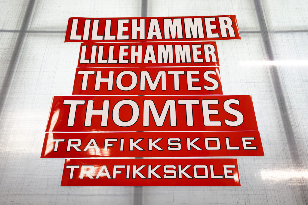 Røde magnetstriper med hvit tekst som viser logoen til Lillehammer Thomtes Trafikkskole.