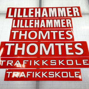 Røde magnetstriper med hvit tekst som viser logoen til Lillehammer Thomtes Trafikkskole.